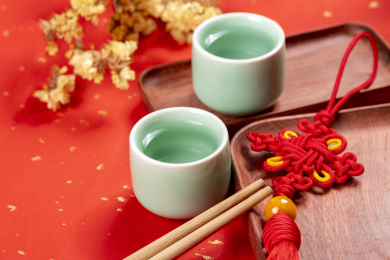梅子青酒壶酒杯摆放在红色洒金背景上旁边放有中国结木托盘