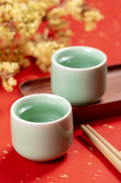 梅子青酒壶酒杯摆放在红色洒金背景上旁边放有中国结木托盘