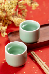 梅子青酒壶酒杯摆放在红色洒金背景上旁边放有中国结木托盘