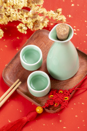 梅子青酒壶酒杯摆放在红色洒金背景上旁边放有中国结木托盘
