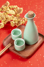 梅子青酒壶酒杯摆放在红色洒金背景上旁边放有中国结木托盘
