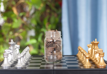 严正以待的国际象棋双方和中间一个装满美元的玻璃瓶
