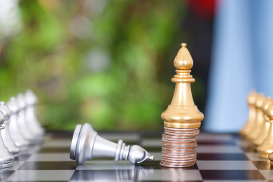 国际象棋棋盘上站在一摞美元硬币上的金色象棋子和失败求饶的银色象棋子