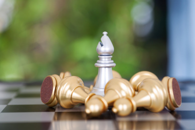 国际象棋棋盘上一枚被一堆金色兵棋子围绕的银色象棋子