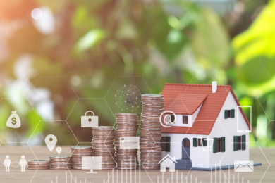 虚化绿植背景前的桌子上一排递增的美元硬币和一个小房子模型