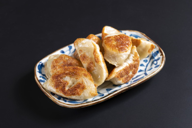 色泽金黄的煎饺子盛放在青花盘子中摆放在黑色背景上旁边放有醋碟筷子蓝花布