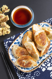 色泽金黄的煎饺子盛放在青花盘子中摆放在黑色背景上旁边放有醋碟筷子蓝花布