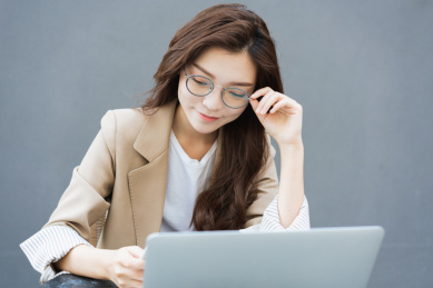 年轻亚洲商务人士一边扶眼镜一边看电脑