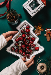 墨绿色背景纸手中捧着的圣诞树形状盘子里装满车厘子