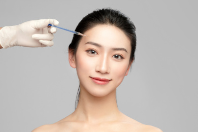  灰色背景里使用针筒的亚洲美女面部特写，化妆护肤整容