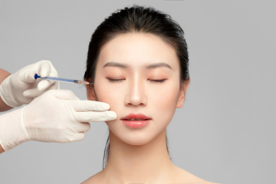  灰色背景里使用针筒的亚洲美女面部特写，化妆护肤整容