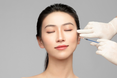  灰色背景里使用针筒的亚洲美女面部特写，化妆护肤整容