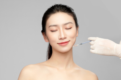  灰色背景里使用针筒的亚洲美女面部特写，化妆护肤整容