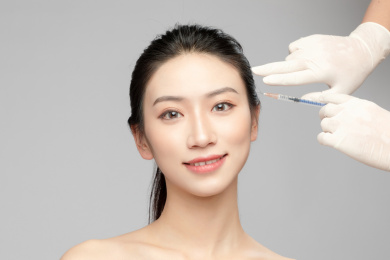  灰色背景里使用针筒的亚洲美女面部特写，化妆护肤整容