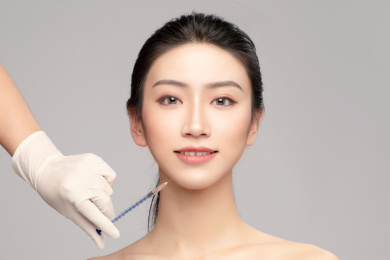  灰色背景里使用针筒的亚洲美女面部特写，化妆护肤整容