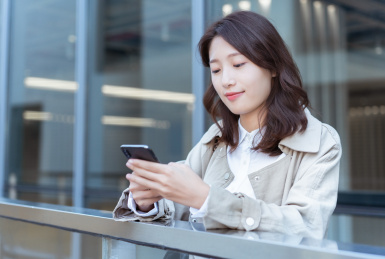 年轻亚洲商务人士靠在栏杆旁玩手机