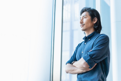 成熟自信的亚洲商务人士双手环抱站在窗边看远方