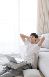 自信的亚洲男青年双手抱头坐在沙发边
