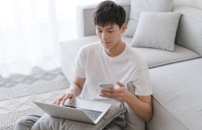 男生坐在客厅的地上依靠着沙发使用笔记本电脑