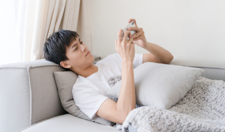 男生一个人躺在沙发上玩手机