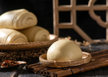 深色背景上竹筐里摆放的手工白面馒头