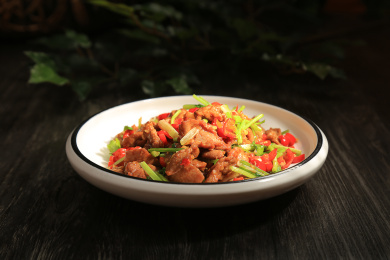 深色木板上一个白色瓷盘中的小炒黄牛肉