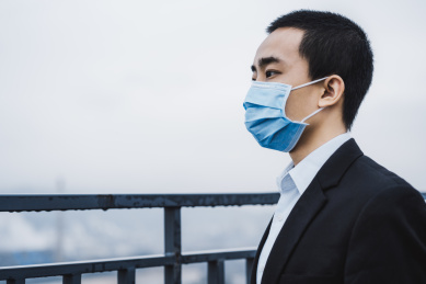 戴着口罩的亚洲商务人士在栏杆旁看远方