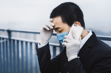 戴着口罩的亚洲商务人士一边扶额一边打电话