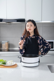 一个年女孩手拿锅铲抵着下巴站在厨房面对镜