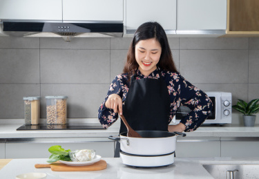 一个女人面带笑容手拿锅铲在厨房做菜