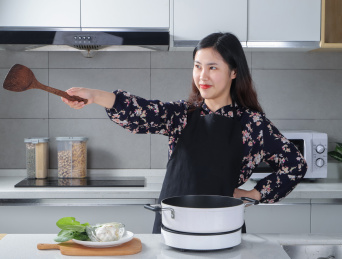 一个女人站在厨房手拿锅铲指向右边