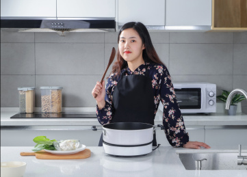 一个女人在厨房桌台前拿着锅铲看镜头微笑