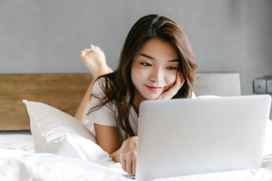 年轻女孩趴在床上使用笔记本电脑