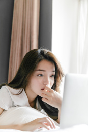 年轻女孩趴在床上使用笔记本电脑