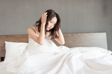 年轻女性坐在床上用手抱着头