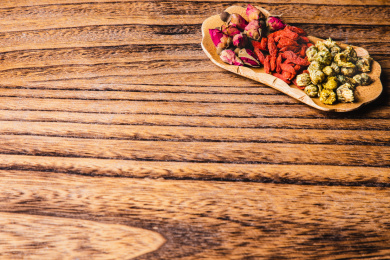 木桌上特写荷叶型木碟子里放着菊花等中草药