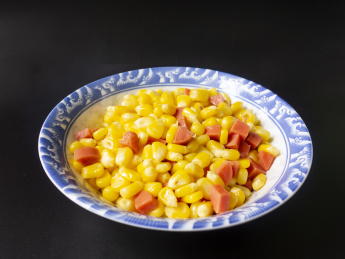 黑色背景中放着一盘玉米炒火腿肠