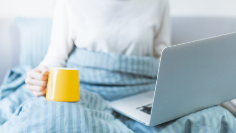 半卧在床的人手捧杯子在看电脑