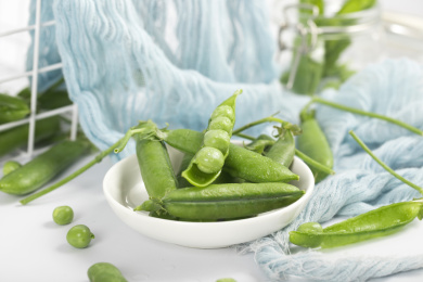 桌子上用白色碟子装着的鲜嫩豌豆荚