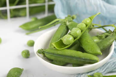 桌子上用白色碟子装着的鲜嫩豌豆荚