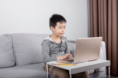 坐在室内沙发上用笔记本电脑学习的儿童