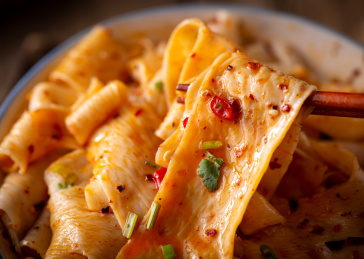 黑色背景上筷子夹起的红油面皮