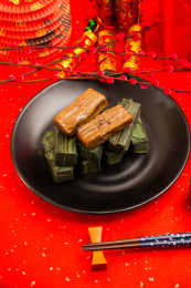 装在黑色盘里的竹叶糯米饭放在红色洒金纸上
