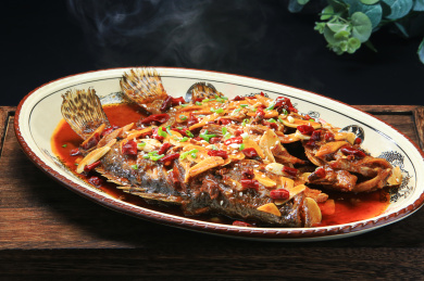 深色木托盘上白色椭圆盘中的秘制丑桂鱼