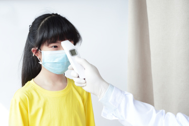 医生用红外线额温枪给戴口罩的女童测量体温