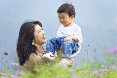 花丛中一个年轻的妈妈抱着小孩玩耍