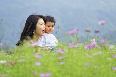 花丛中一个年轻的妈妈抱着小孩玩耍