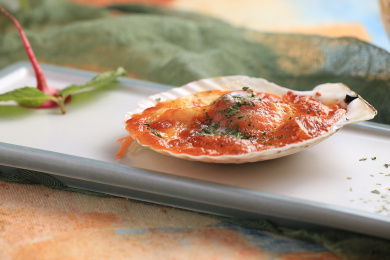 橙色桌布上白色长盘上的芝士扇贝特写