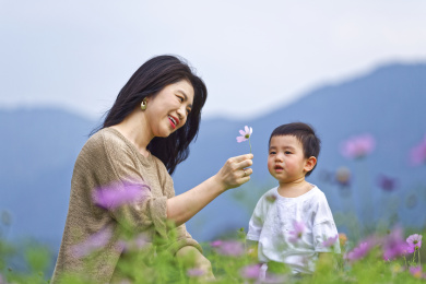 一个年轻的妈妈陪小男孩在花从里玩耍