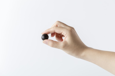 白色背景一只手拿着一颗中成药药丸特写